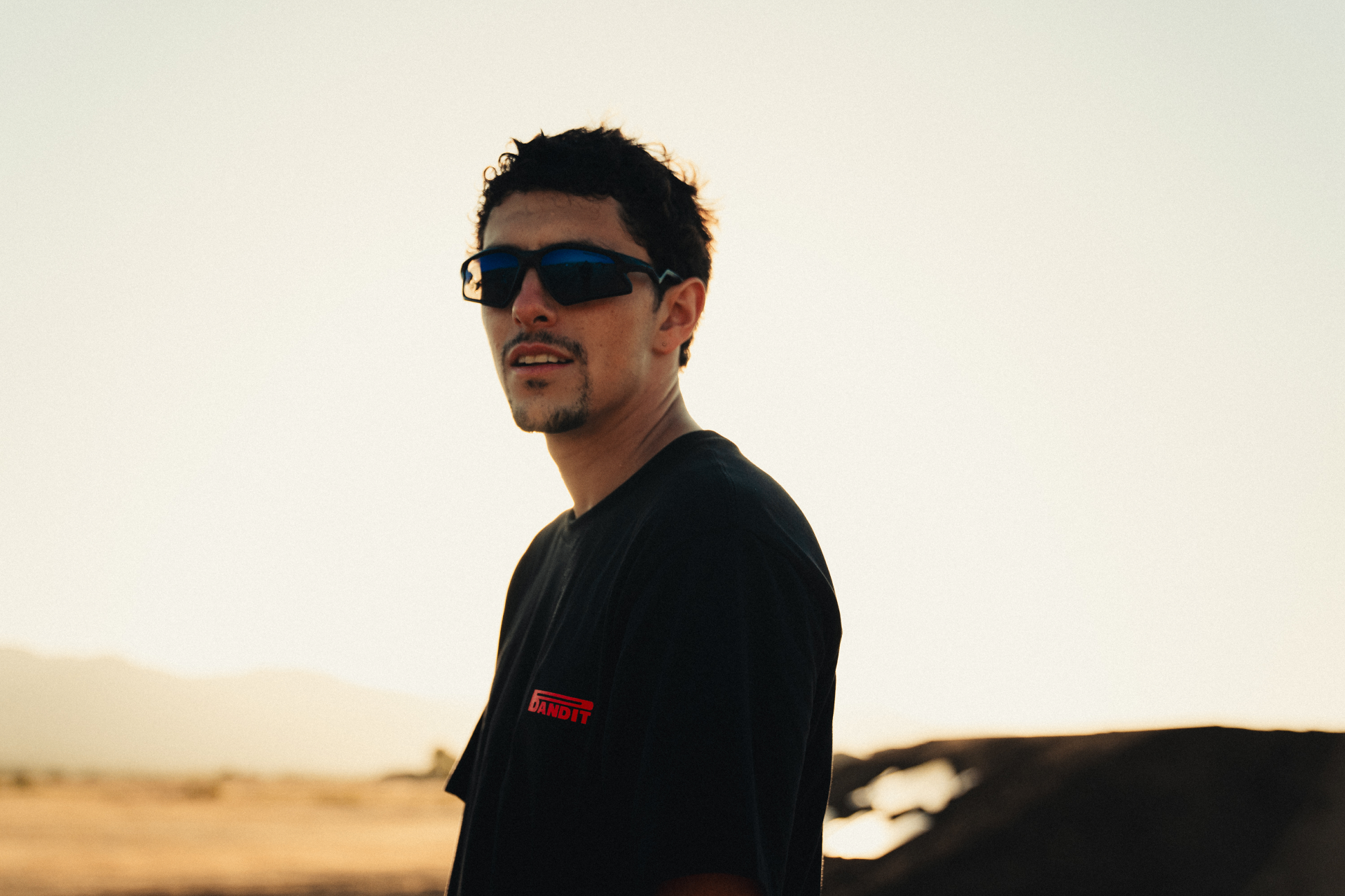 Portrait of a person in a black Bandit tee and sunglasses at golden hour in the desert