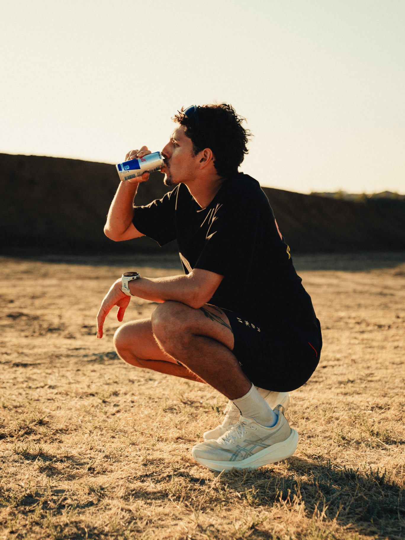 Runner crouched in the desert sipping a Red Bull at golden hour
