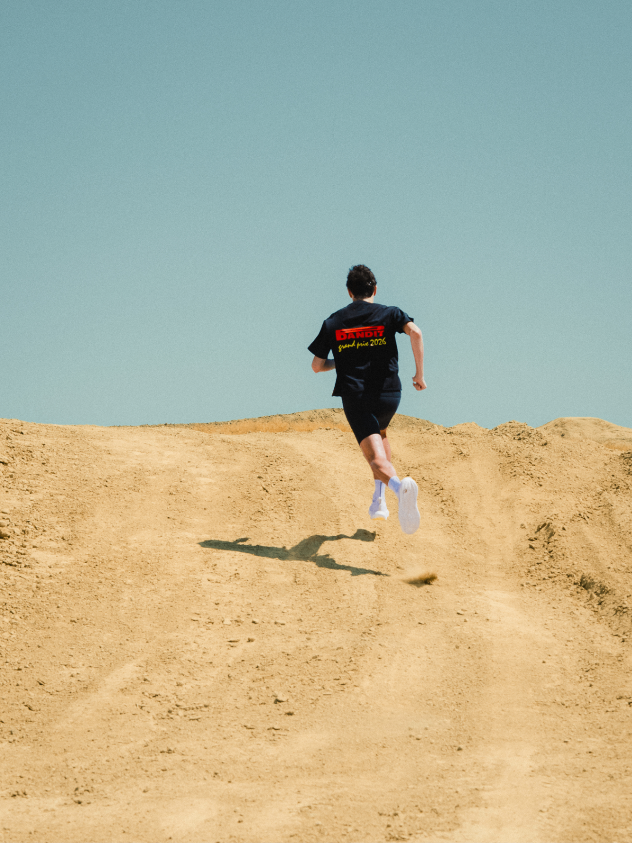 Runner in a Bandit Grand Prix 2026 tee sprinting up a sandy hill