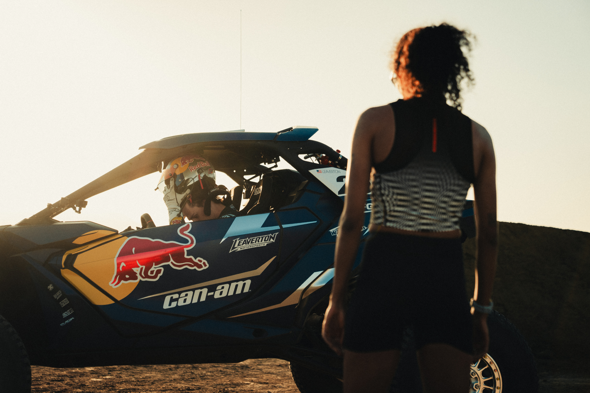 Runner approaching a Red Bull Can-Am buggy with the driver seated inside at sunset