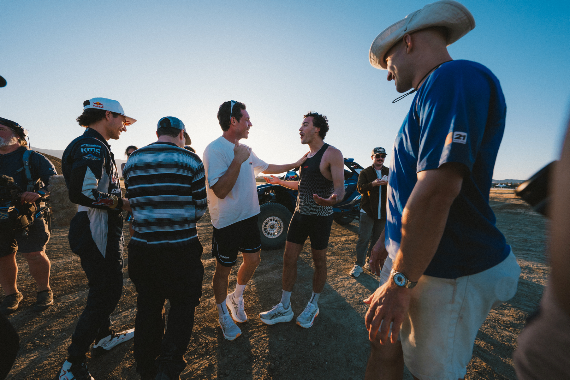 Runners and crew talking beside a Red Bull Can-Am buggy at golden hour