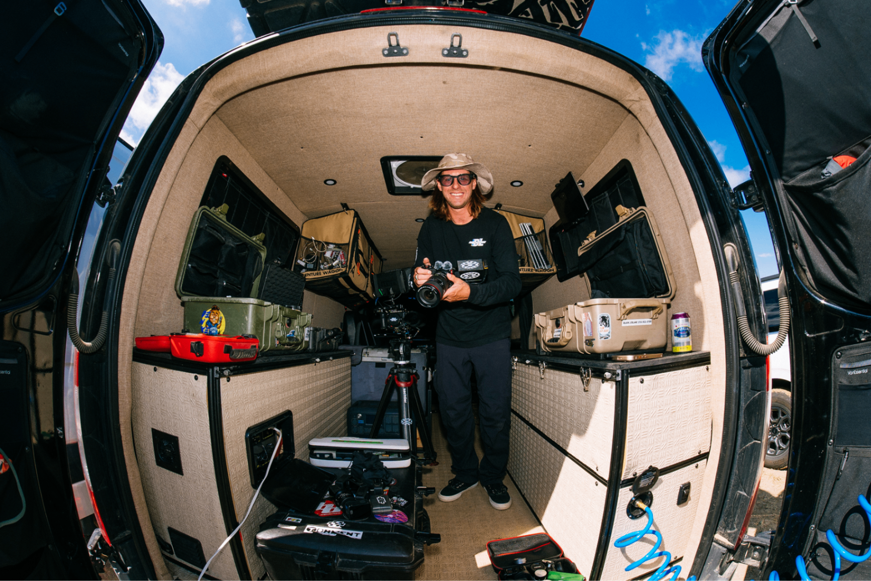 Photographer holding a camera inside a gear-packed adventure van at the Bandit Grand Prix