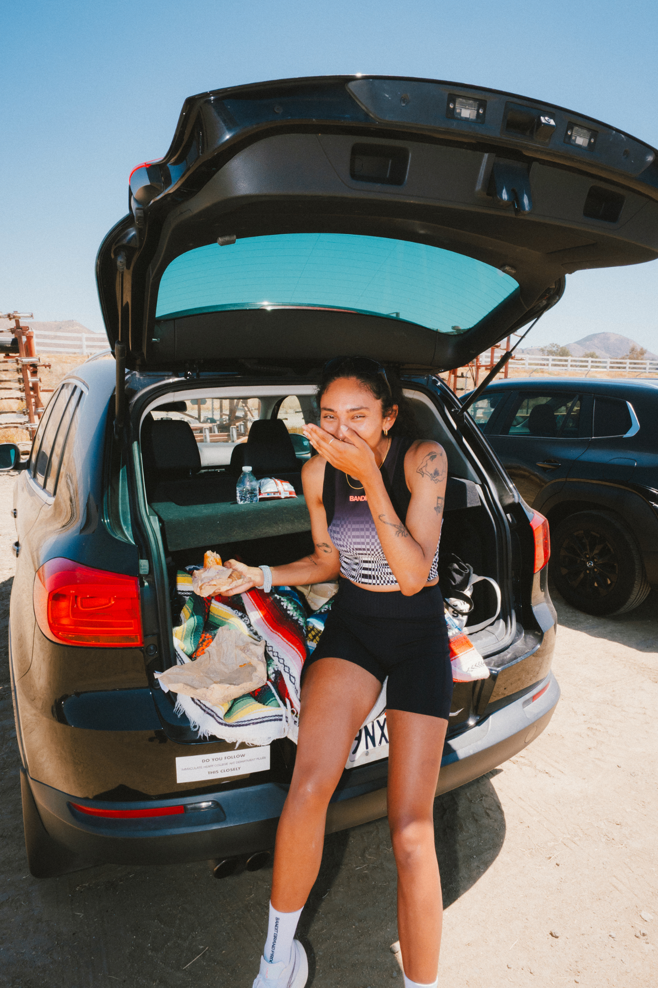 Runner laughing while holding a burrito at the back of an SUV in the desert