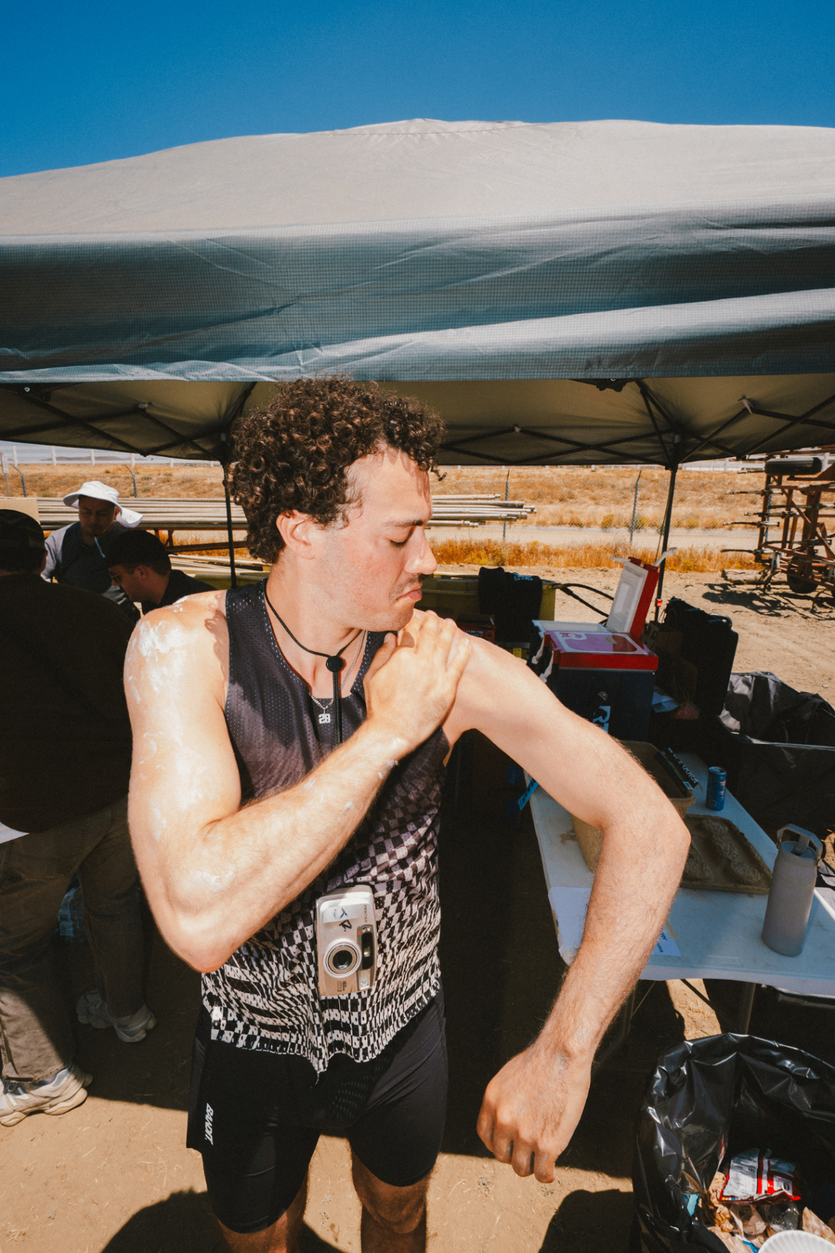 Runner applying sunscreen under a pop-up tent with a film camera around his neck