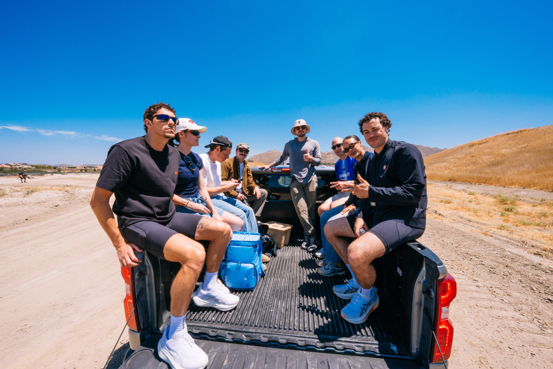Group riding in the back of a pickup truck through the desert under a bright blue sky