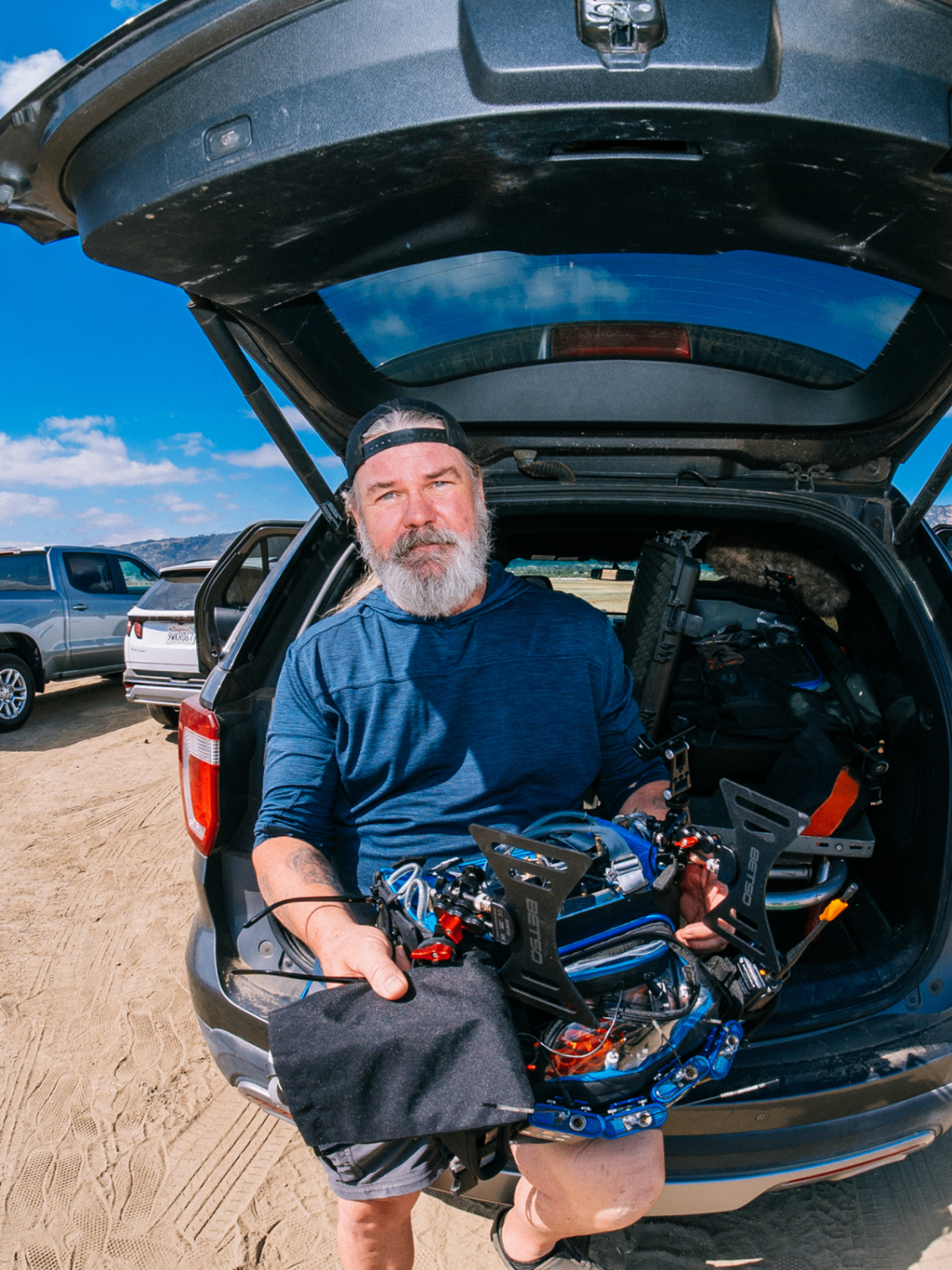 Crew member holding a rigged camera stabilizer at the back of an SUV in the desert