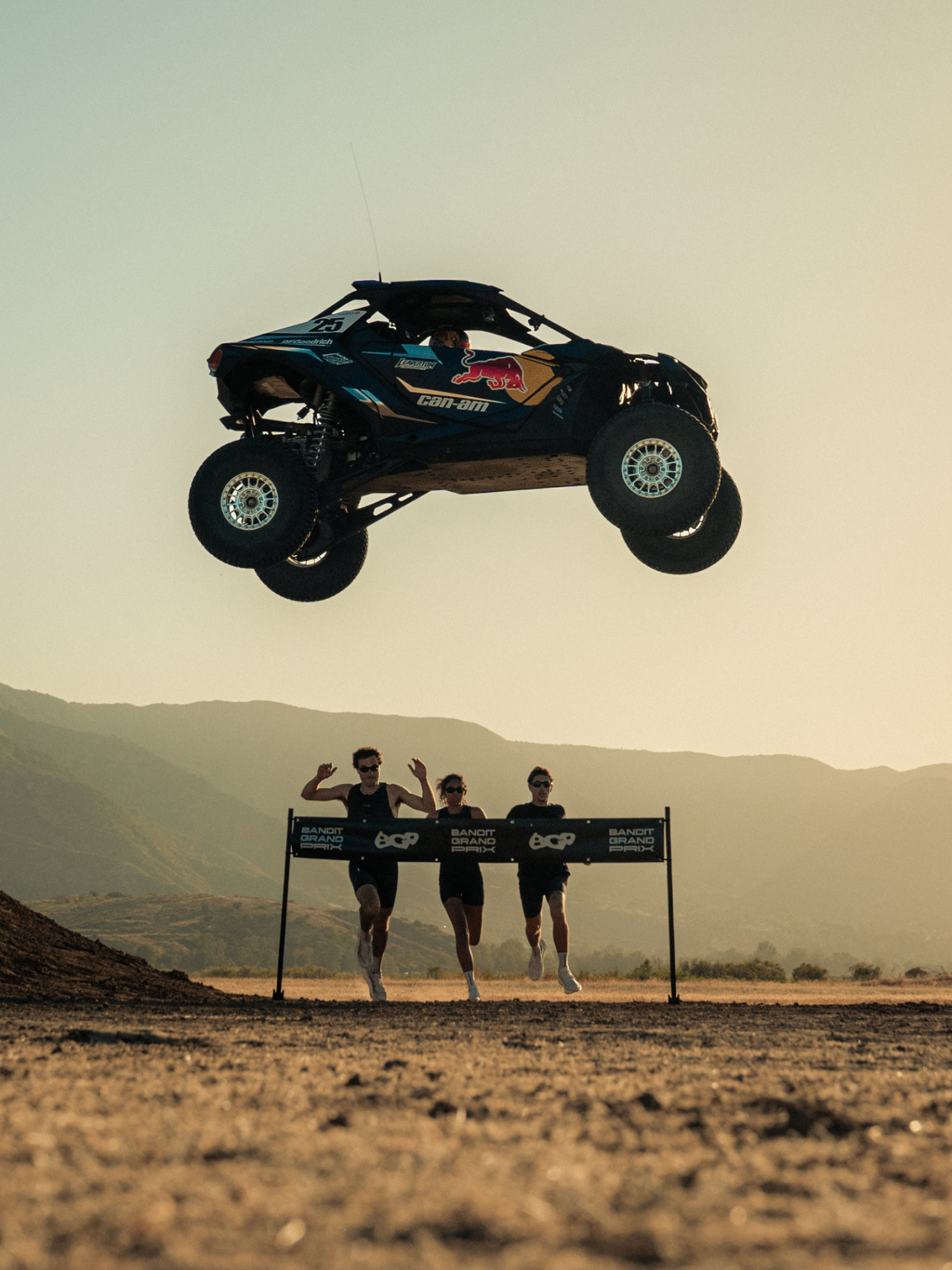 Can-Am Red Bull buggy soaring over runners with mountains in the background