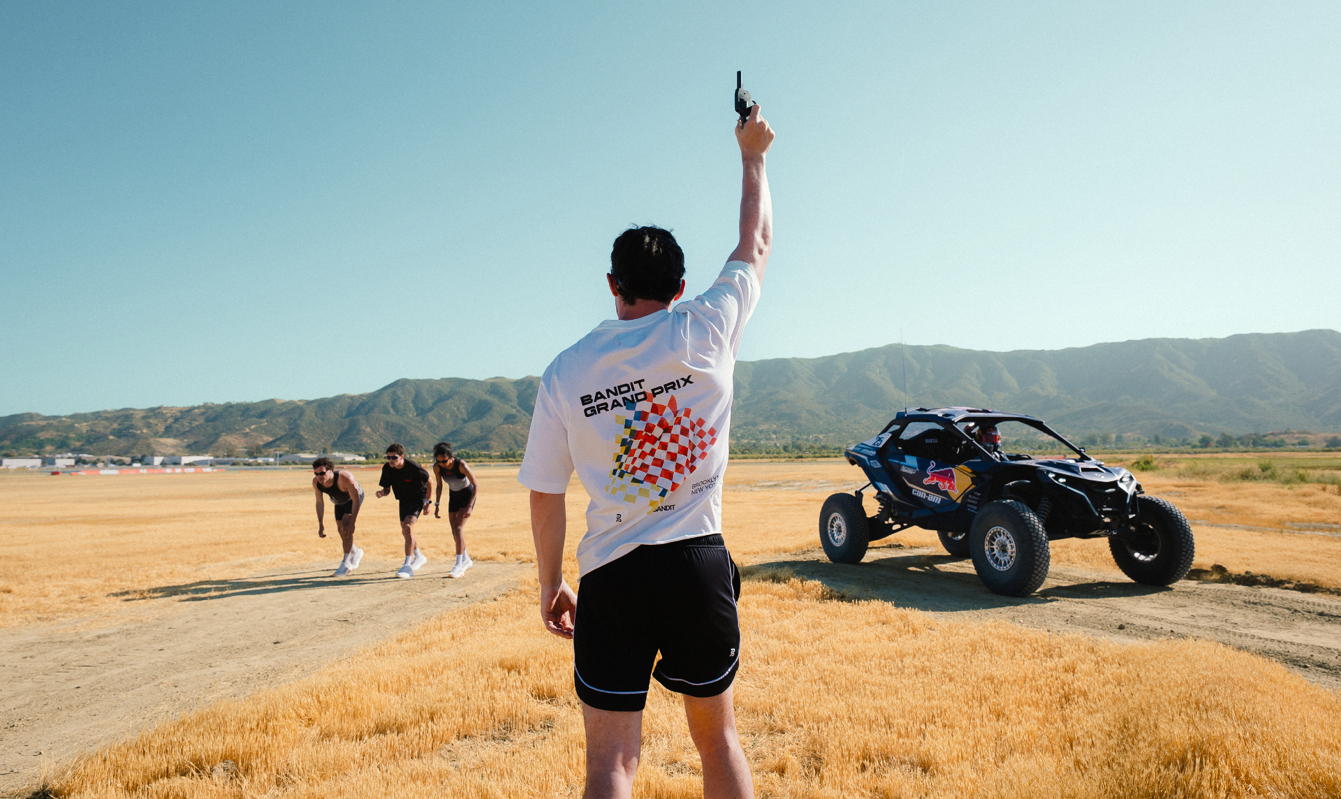 Race starter raising a pistol as runners line up beside a Can-Am buggy