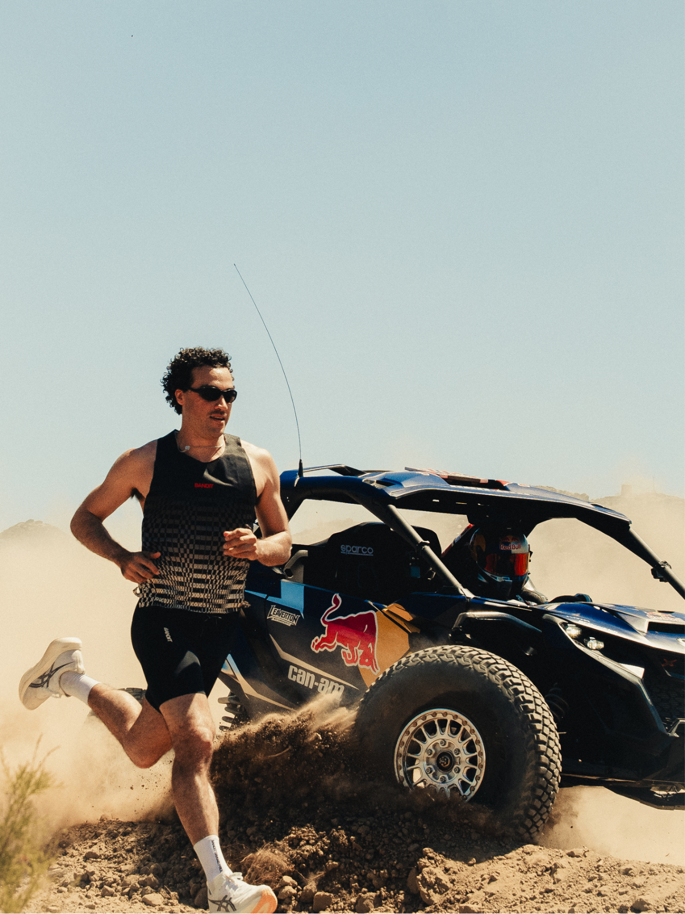Runner beside a Red Bull Can-Am buggy kicking up dust in the desert